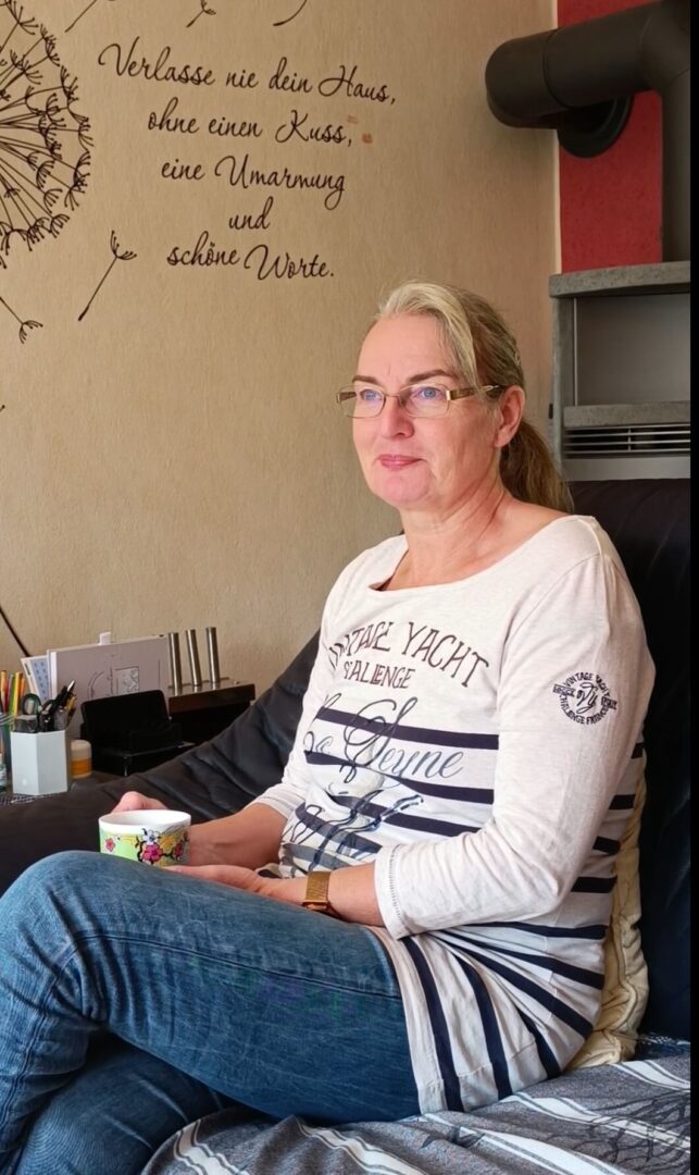 Andrea Oeing sitzt entspannt auf dem Sofa mit einer Tasse Tee in der Hand – ein Moment der Ruhe und Achtsamkeit im Alltag, der zeigt, wie wichtig kleine Pausen sind.