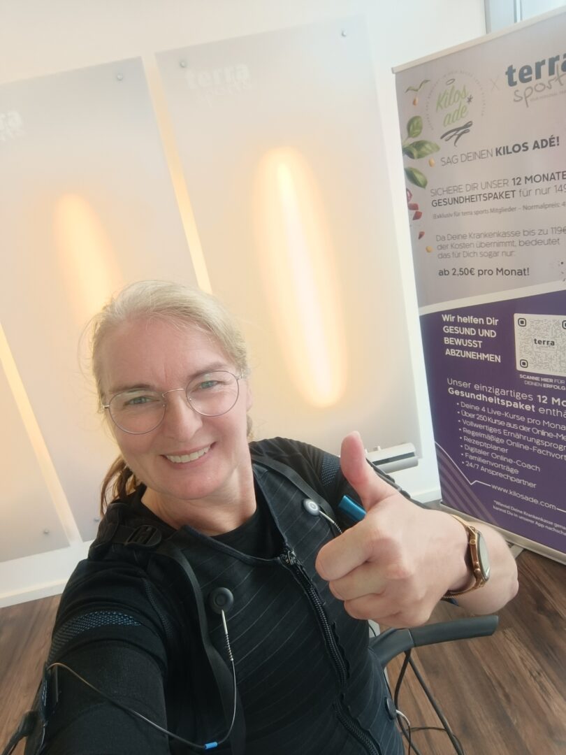 Andrea Oeing lächelt in die Kamera und zeigt den Daumen hoch während eines EMS-Trainings. Ein Moment voller Energie, Motivation und Lebensfreude.