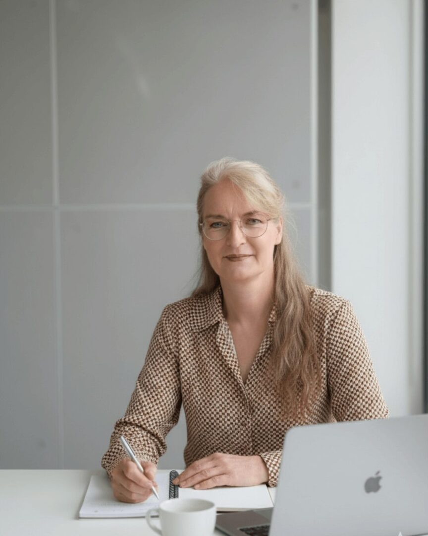 Frau sitzt am Tisch und blickt in ein Planungsbuch mit den Spalten Monat, Woche und Fokus – ruhige Szene für realistische Alltagsplanung